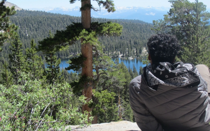 a person rests on a rock overlooking trees and a body of water on an outward bound course for bipoc